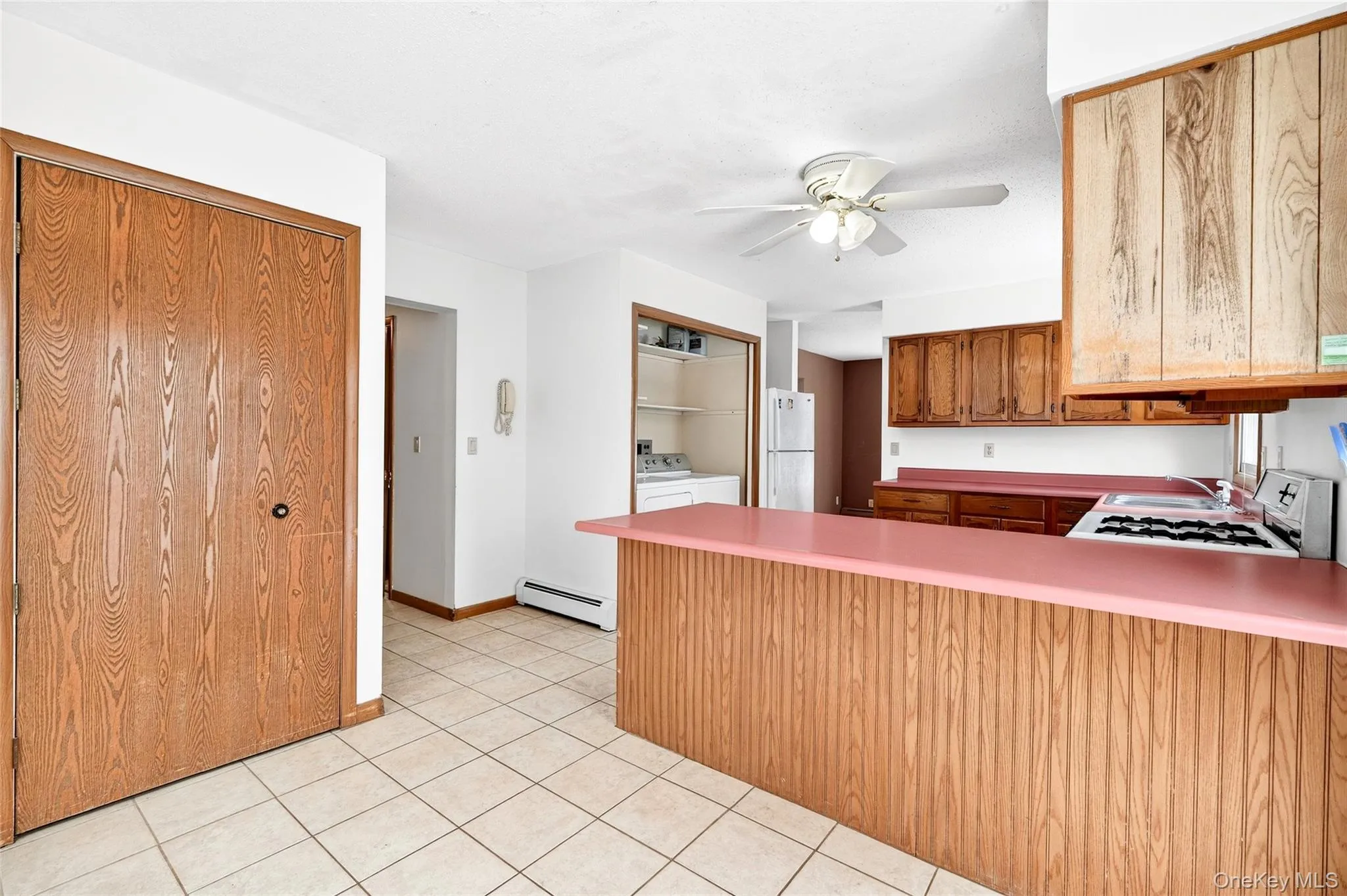 Kitchen featuring a peninsula, white appliances, light countertops, a baseboard heating unit, and brown cabinets Kitchen featuring a peninsula, white appliances, light countertops, a baseboard heating unit, and brown cabinets