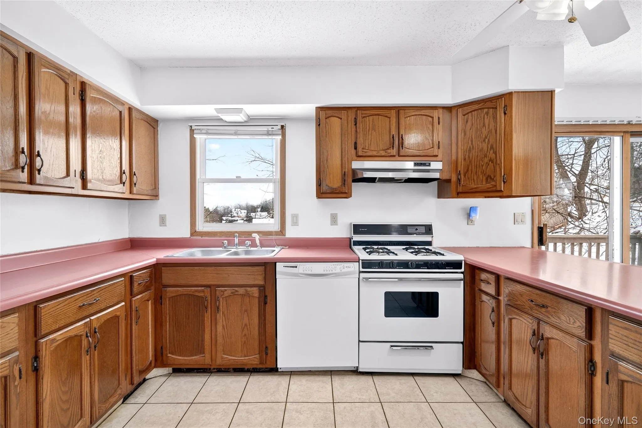 Kitchen featuring white appliances, brown cabinets, a textured ceiling, under cabinet range hood, and light countertops Kitchen featuring white appliances, brown cabinets, a textured ceiling, under cabinet range hood, and light countertops