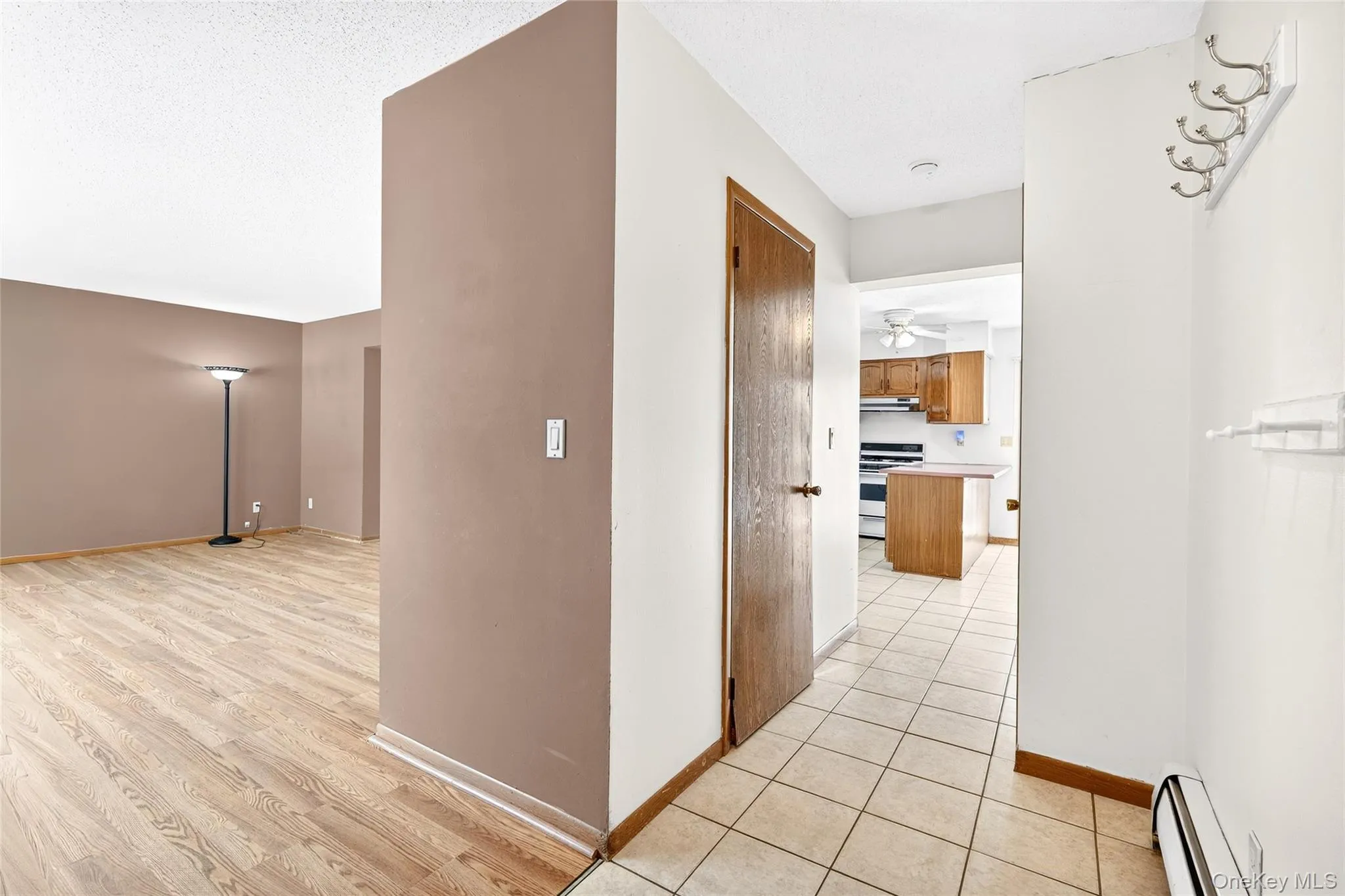 Hallway featuring a baseboard heating unit, light wood-type flooring, and a textured ceiling Hallway featuring a baseboard heating unit, light wood-type flooring, and a textured ceiling