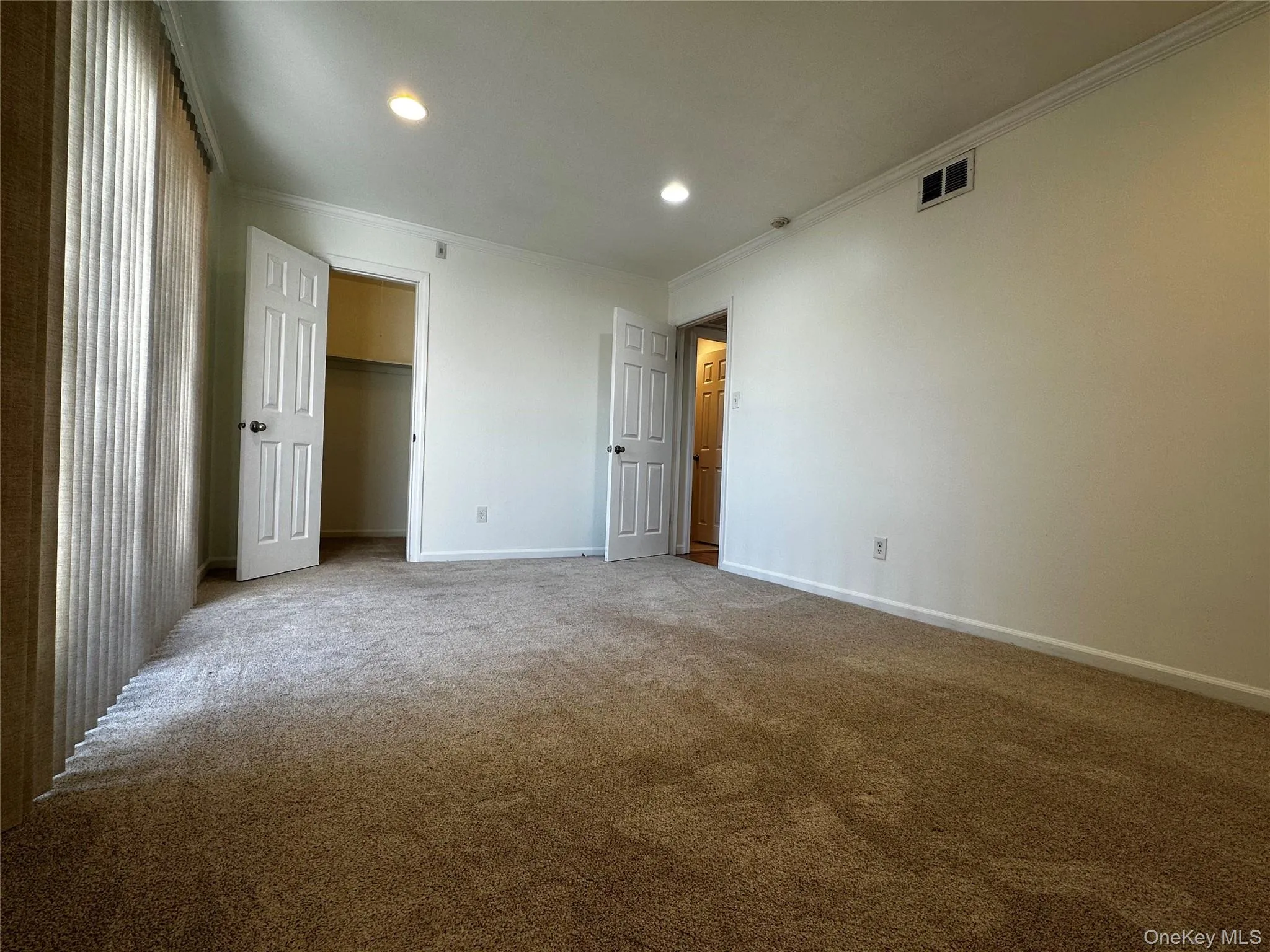 Unfurnished bedroom with carpet floors, recessed lighting, ornamental molding, and a walk in closet Unfurnished bedroom with carpet floors, recessed lighting, ornamental molding, and a walk in closet