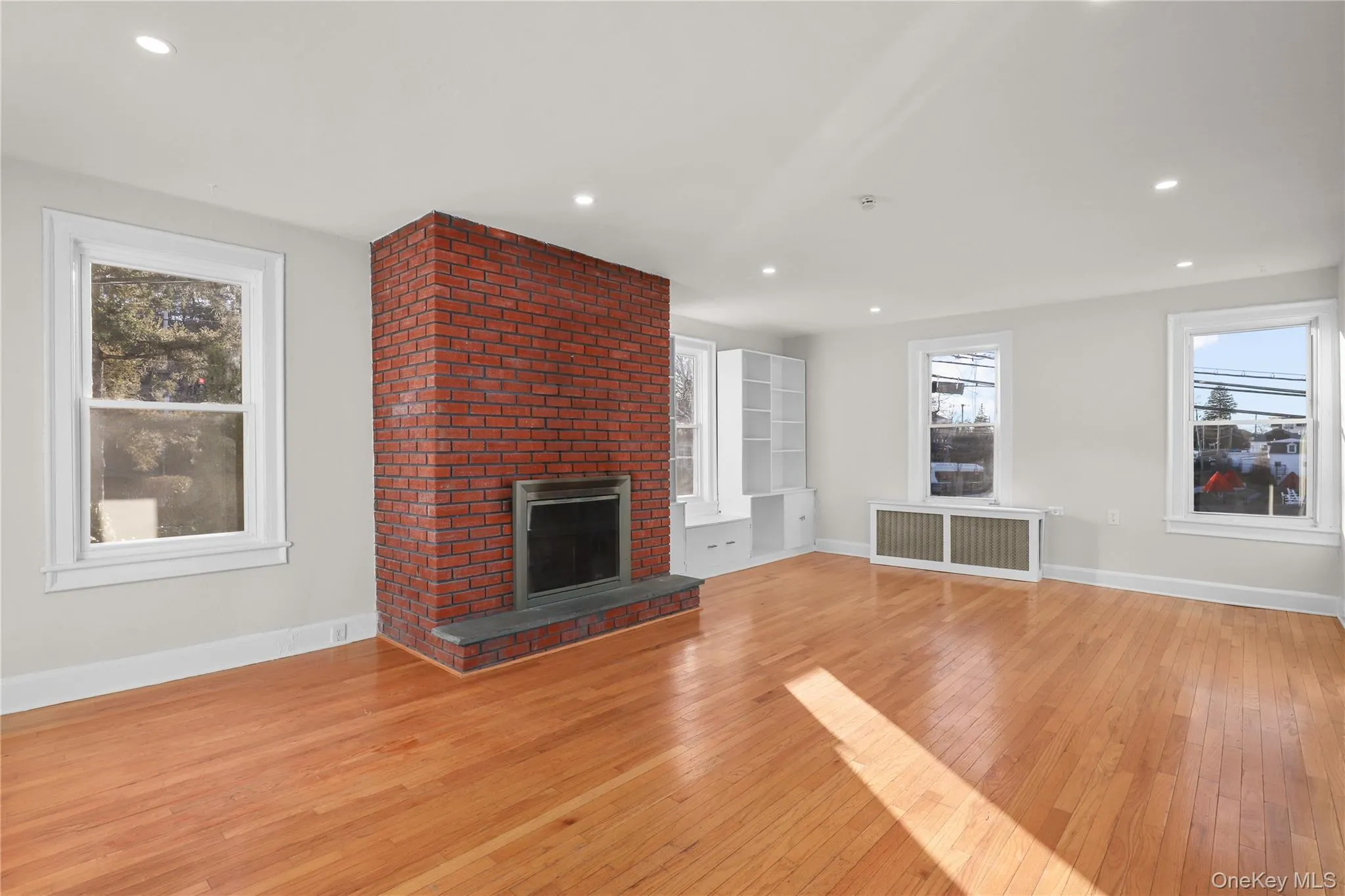 Unfurnished living room featuring light wood-type flooring, a fireplace, radiator heating unit, and recessed lighting Unfurnished living room featuring light wood-type flooring, a fireplace, radiator heating unit, and recessed lighting