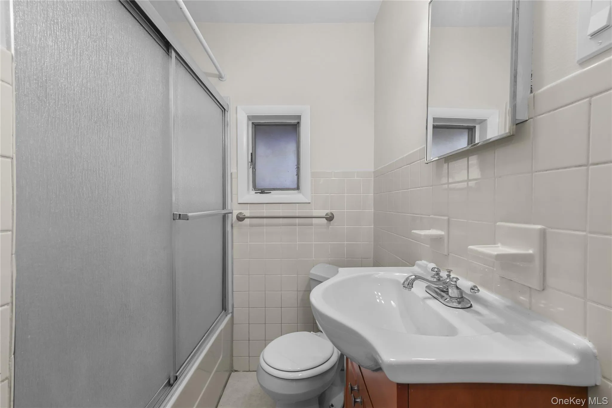 Full bath with vanity, combined bath / shower with glass door, tile walls, and a wainscoted wall Full bath with vanity, combined bath / shower with glass door, tile walls, and a wainscoted wall