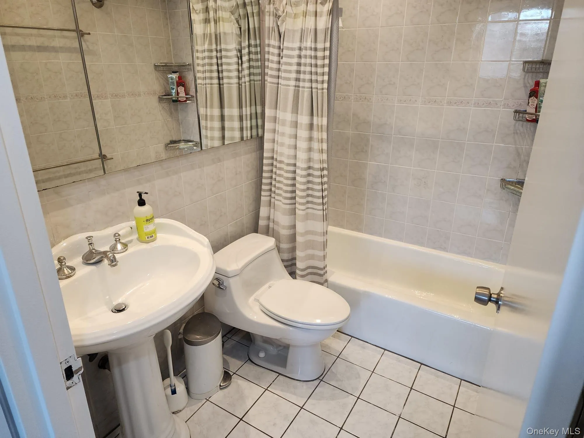 Full bath with tile walls, shower / bath combo, and light tile patterned floors Full bath with tile walls, shower / bath combo, and light tile patterned floors