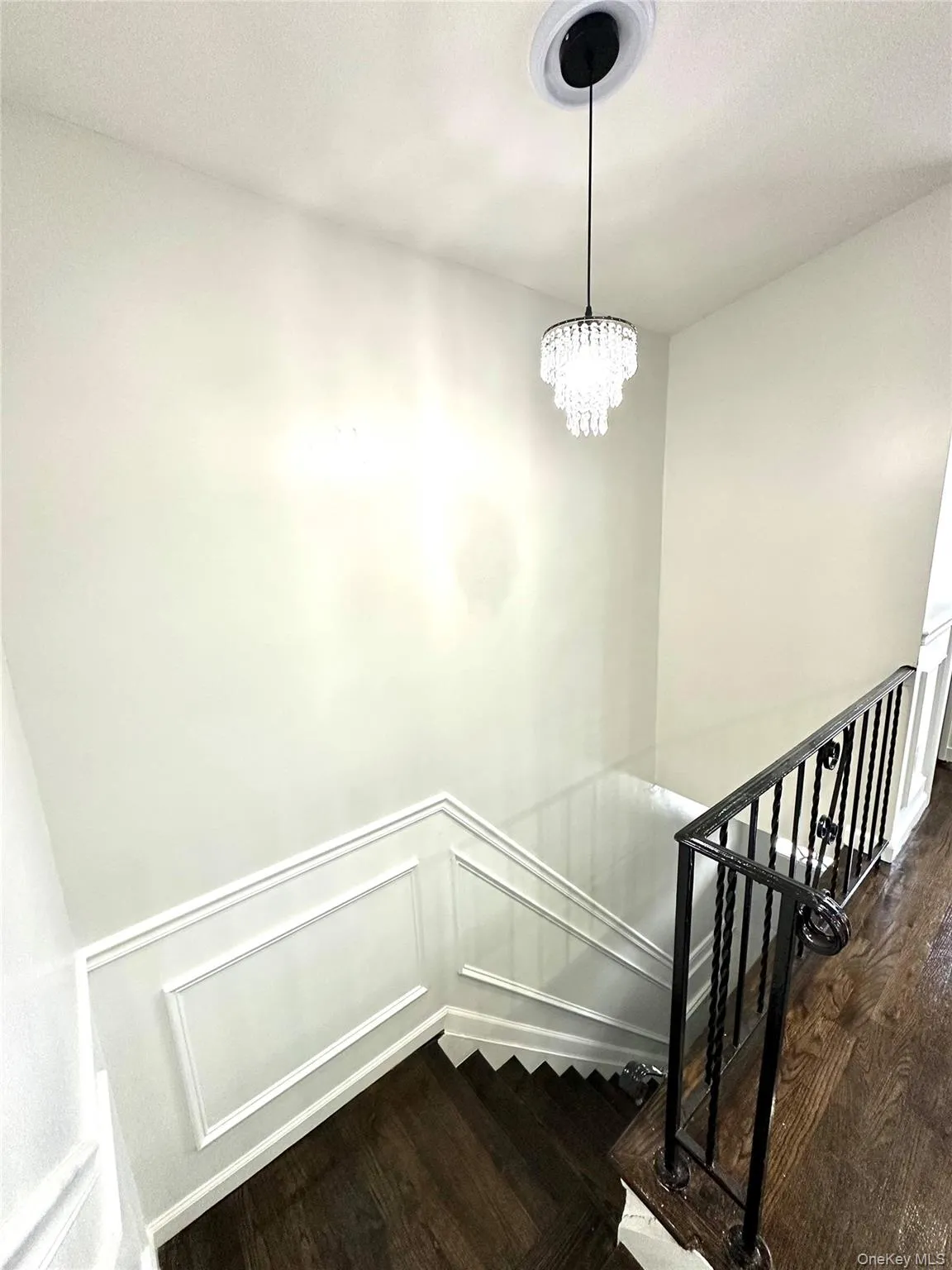 Stairs with a decorative wall, wood finished floors, a wainscoted wall, a chandelier, and a textured ceiling Stairs with a decorative wall, wood finished floors, a wainscoted wall, a chandelier, and a textured ceiling