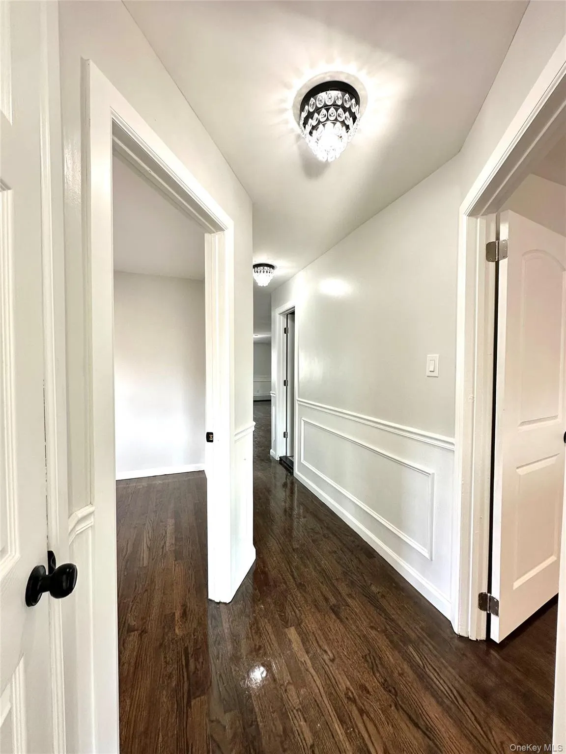 Corridor with dark wood-style floors, a decorative wall, and wainscoting Corridor with dark wood-style floors, a decorative wall, and wainscoting