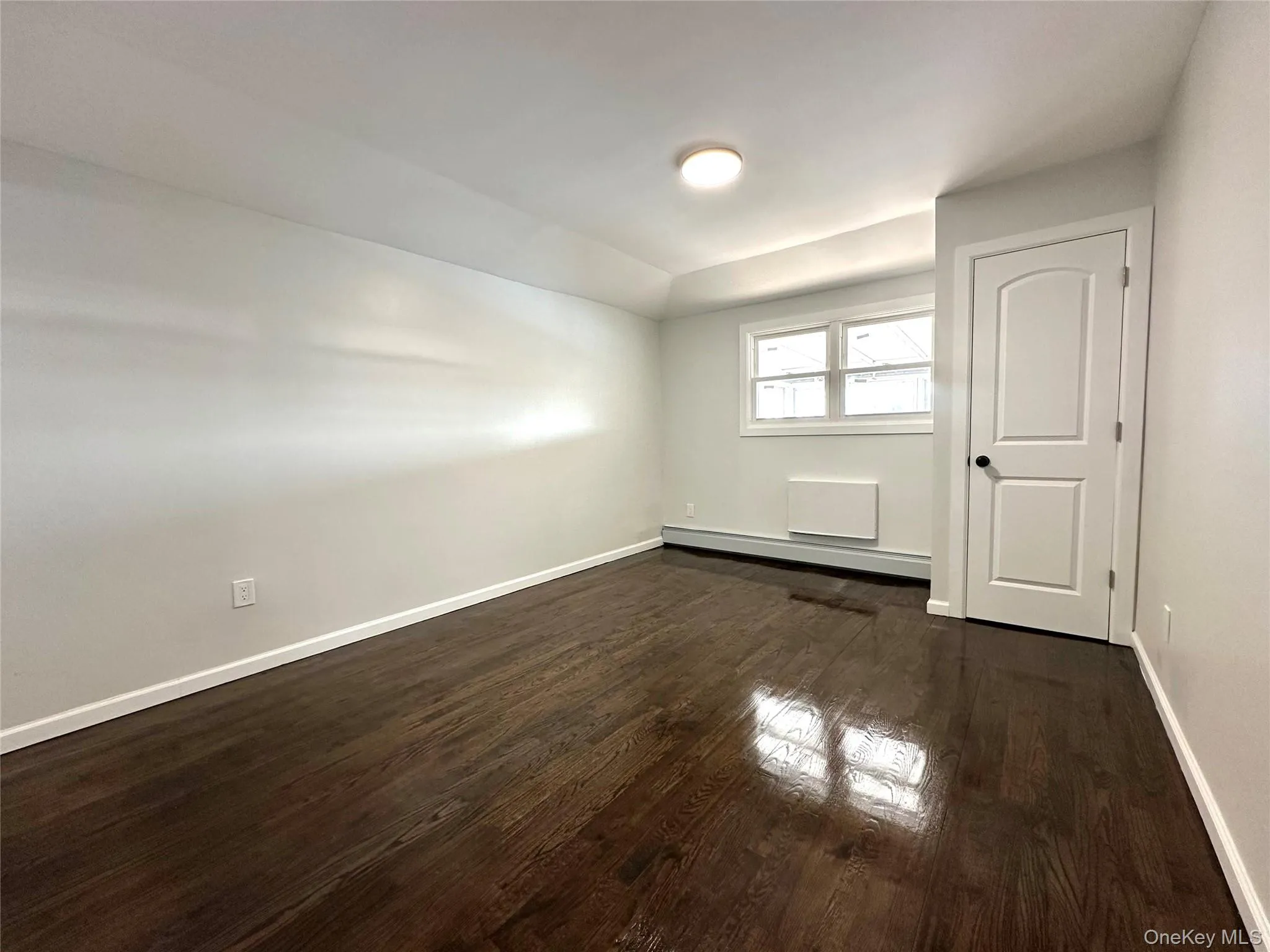 Unfurnished room with dark wood finished floors and a baseboard heating unit Unfurnished room with dark wood finished floors and a baseboard heating unit