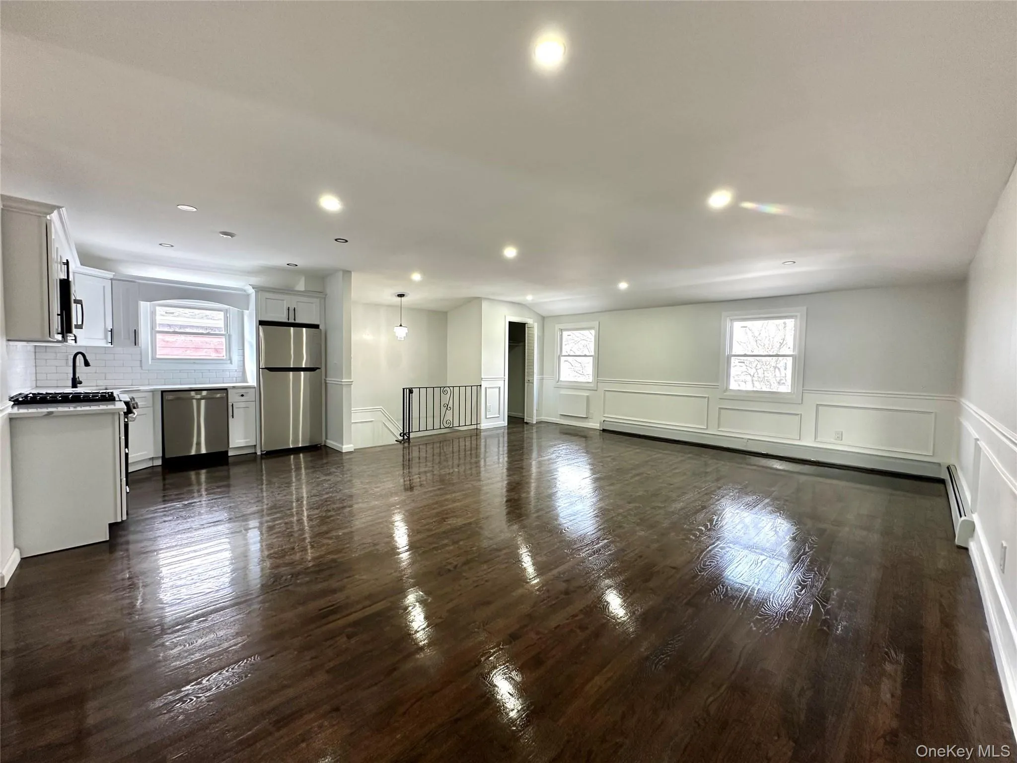 Unfurnished living room featuring a decorative wall, a wainscoted wall, healthy amount of natural light, dark wood finished floors, and a baseboard radiator Unfurnished living room featuring a decorative wall, a wainscoted wall, healthy amount of natural light, dark wood finished floors, and a baseboard radiator