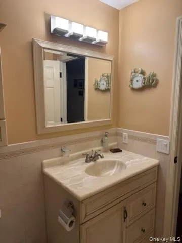 Half bath featuring a wainscoted wall, tile walls, and vanity Half bath featuring a wainscoted wall, tile walls, and vanity