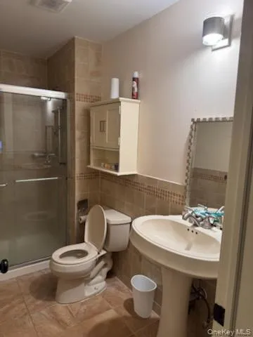 Bathroom with tile walls, a shower stall, light tile patterned floors, and a wainscoted wall Bathroom with tile walls, a shower stall, light tile patterned floors, and a wainscoted wall