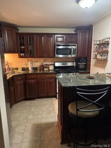 Kitchen with a kitchen breakfast bar, stainless steel appliances, dark brown cabinets, glass insert cabinets, and dark stone countertops Kitchen with a kitchen breakfast bar, stainless steel appliances, dark brown cabinets, glass insert cabinets, and dark stone countertops