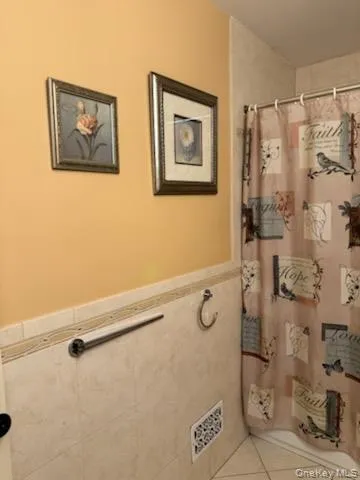 Bathroom with a shower with shower curtain, tile patterned floors, and wainscoting Bathroom with a shower with shower curtain, tile patterned floors, and wainscoting
