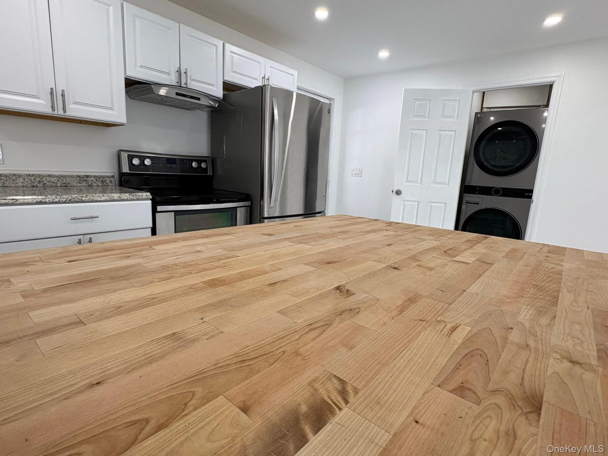 Kitchen with butcher block countertops, appliances with stainless steel finishes, white cabinetry, under cabinet range hood, and recessed lighting Kitchen with butcher block countertops, appliances with stainless steel finishes, white cabinetry, under cabinet range hood, and recessed lighting