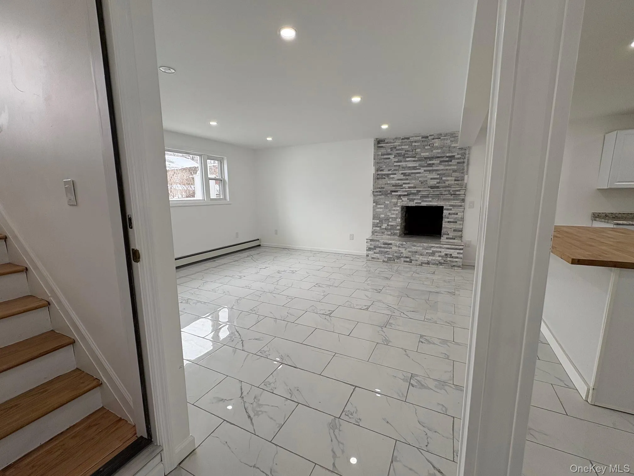 Unfurnished living room with light marble finish floors, a large fireplace, stairs, a baseboard radiator, and recessed lighting Unfurnished living room with light marble finish floors, a large fireplace, stairs, a baseboard radiator, and recessed lighting