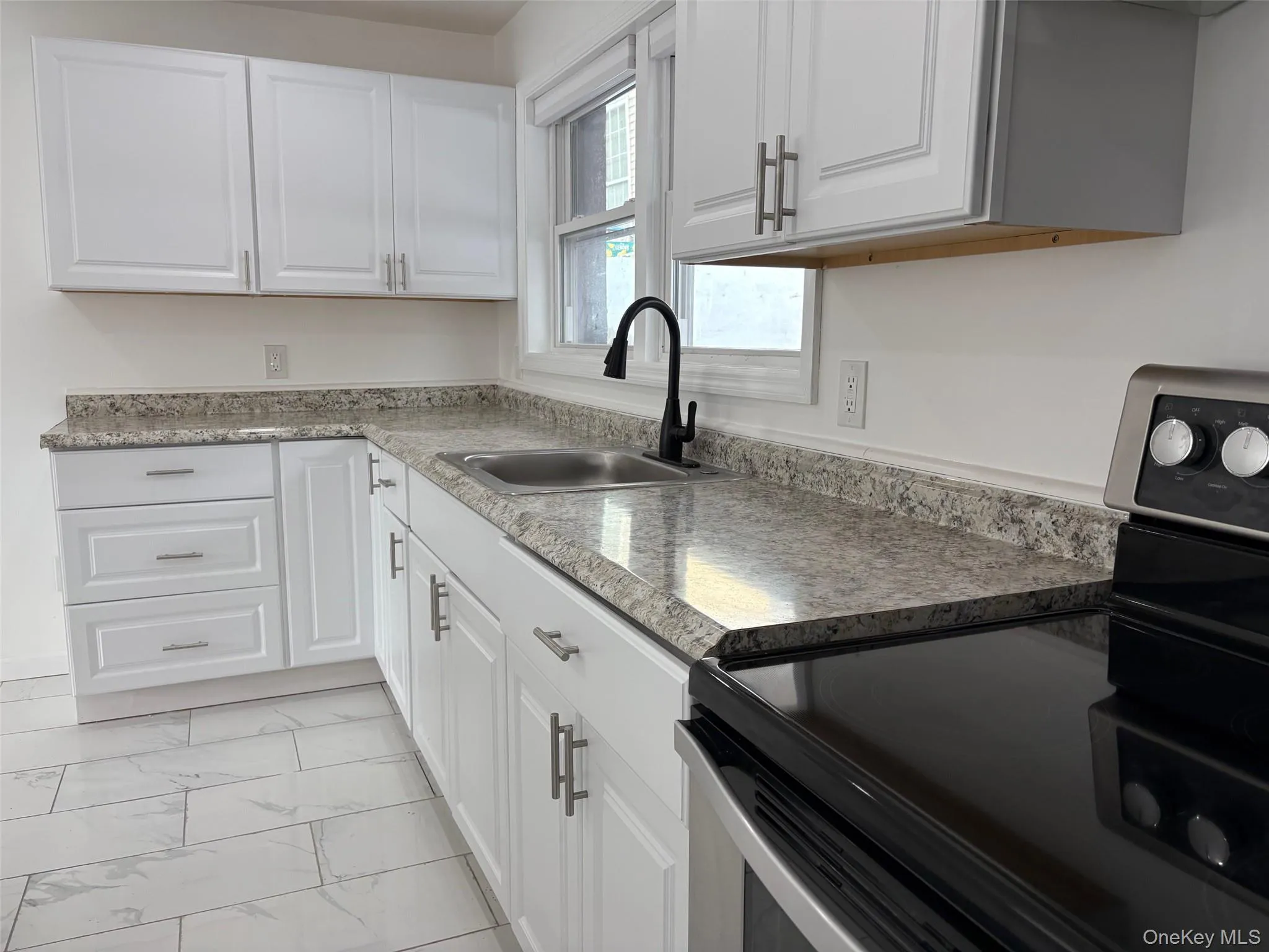 Kitchen with stainless steel electric range, white cabinets, light marble finish floors, and light countertops Kitchen with stainless steel electric range, white cabinets, light marble finish floors, and light countertops