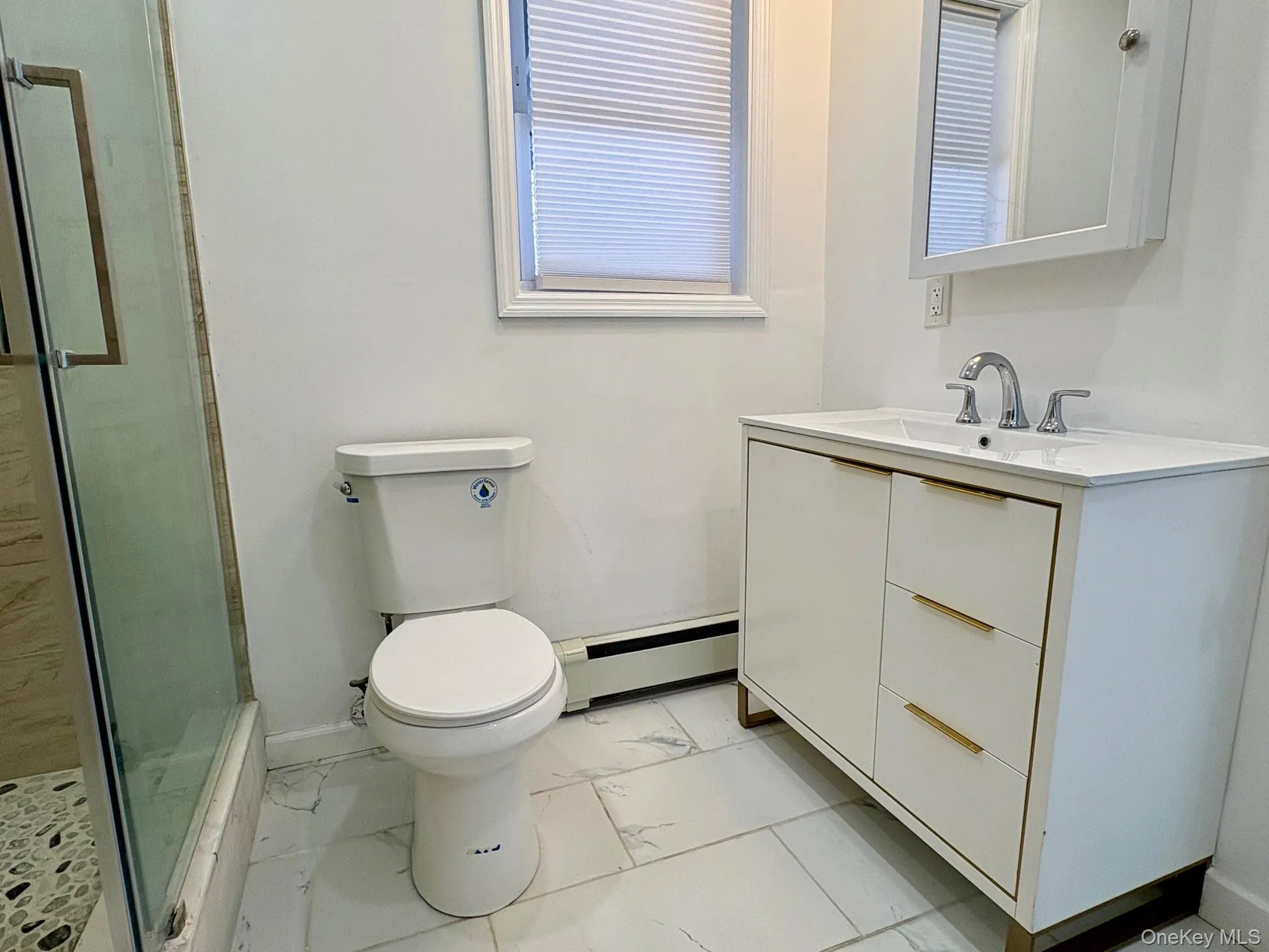Bathroom with a baseboard heating unit, vanity, light marble finish flooring, and a stall shower Bathroom with a baseboard heating unit, vanity, light marble finish flooring, and a stall shower
