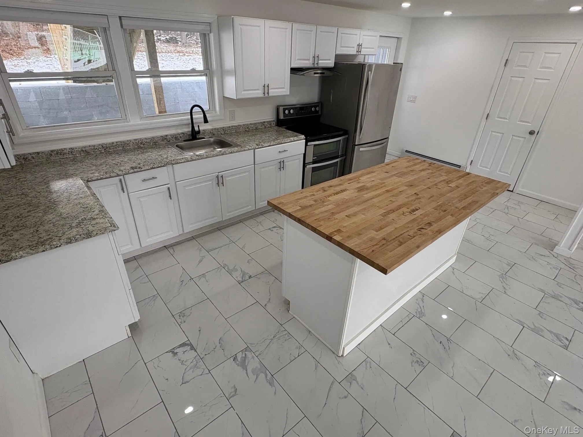 Kitchen with white cabinetry, range with two ovens, light marble finish flooring, a kitchen island, and light stone countertops Kitchen with white cabinetry, range with two ovens, light marble finish flooring, a kitchen island, and light stone countertops