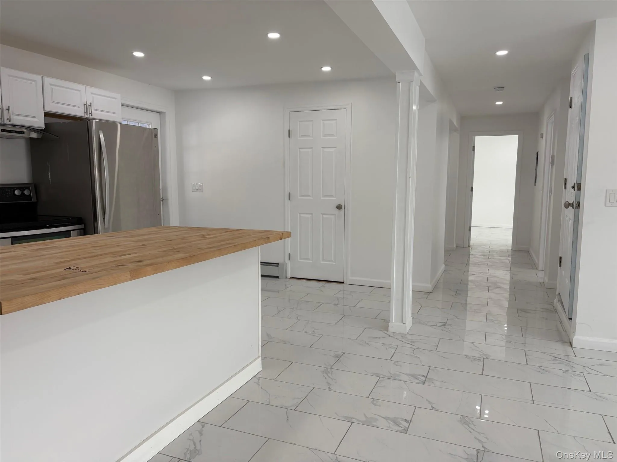 Kitchen featuring butcher block counters, appliances with stainless steel finishes, white cabinetry, recessed lighting, and light marble finish floors Kitchen featuring butcher block counters, appliances with stainless steel finishes, white cabinetry, recessed lighting, and light marble finish floors