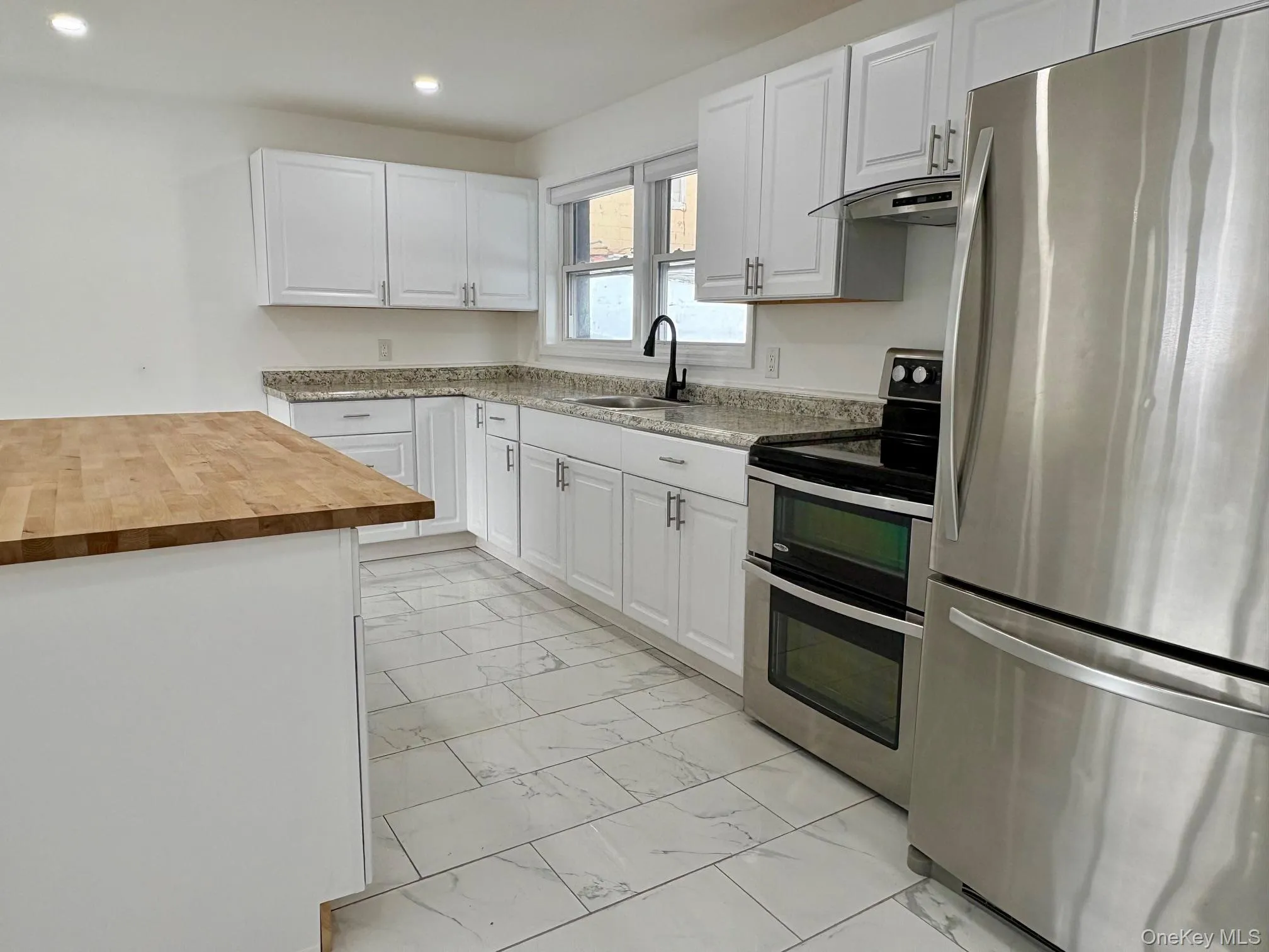 Kitchen with appliances with stainless steel finishes, butcher block counters, white cabinets, light marble finish flooring, and recessed lighting Kitchen with appliances with stainless steel finishes, butcher block counters, white cabinets, light marble finish flooring, and recessed lighting