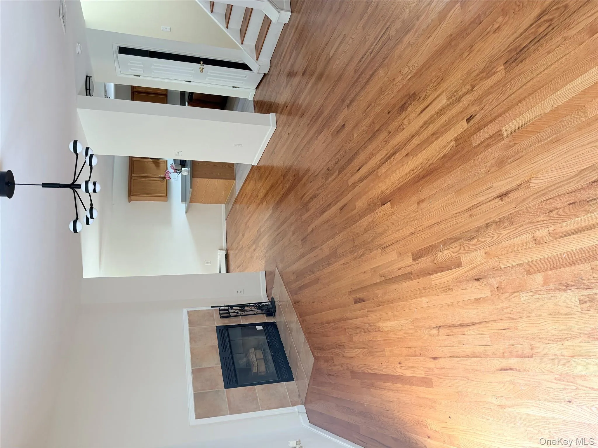 Unfurnished living room with a fireplace, light wood-style flooring, a chandelier, baseboard heating, and stairs Unfurnished living room with a fireplace, light wood-style flooring, a chandelier, baseboard heating, and stairs