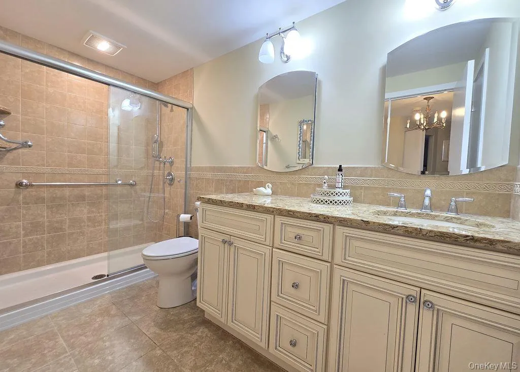 Bathroom featuring double vanity, wainscoting, a stall shower, tile walls, and a chandelier Bathroom featuring double vanity, wainscoting, a stall shower, tile walls, and a chandelier
