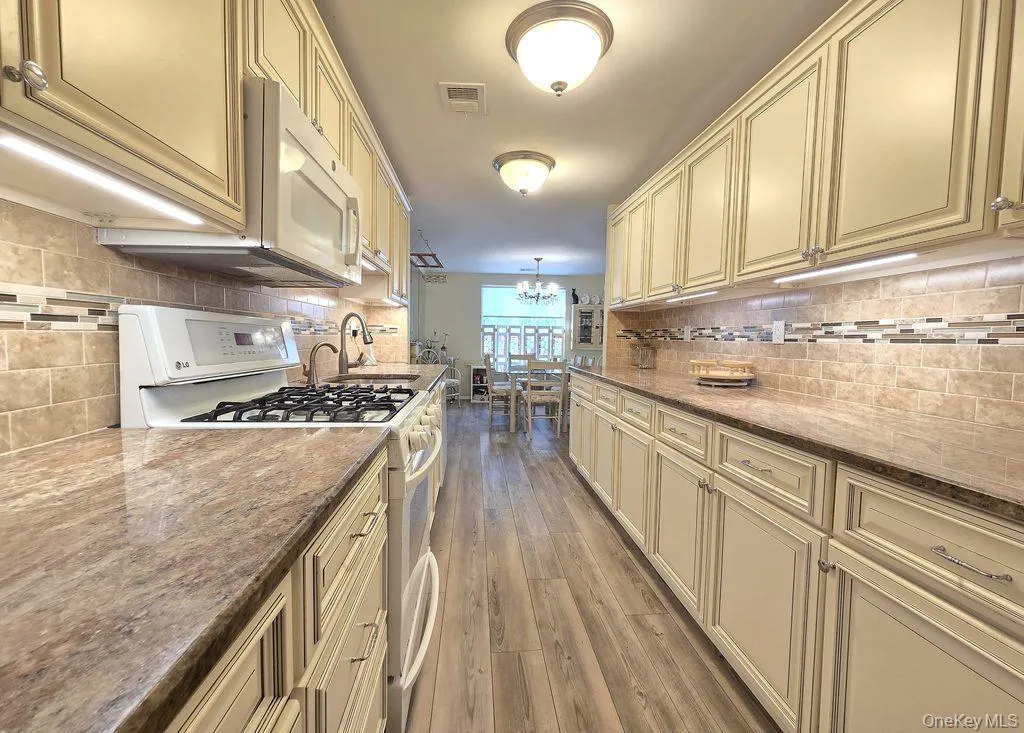 Kitchen with cream cabinets, white appliances, backsplash, and dark stone countertops Kitchen with cream cabinets, white appliances, backsplash, and dark stone countertops