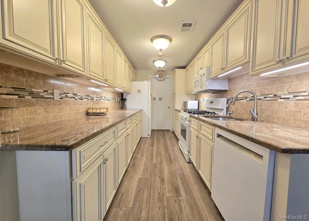 Kitchen featuring white appliances, dark stone counters, light wood-style floors, decorative backsplash, and cream cabinetry Kitchen featuring white appliances, dark stone counters, light wood-style floors, decorative backsplash, and cream cabinetry