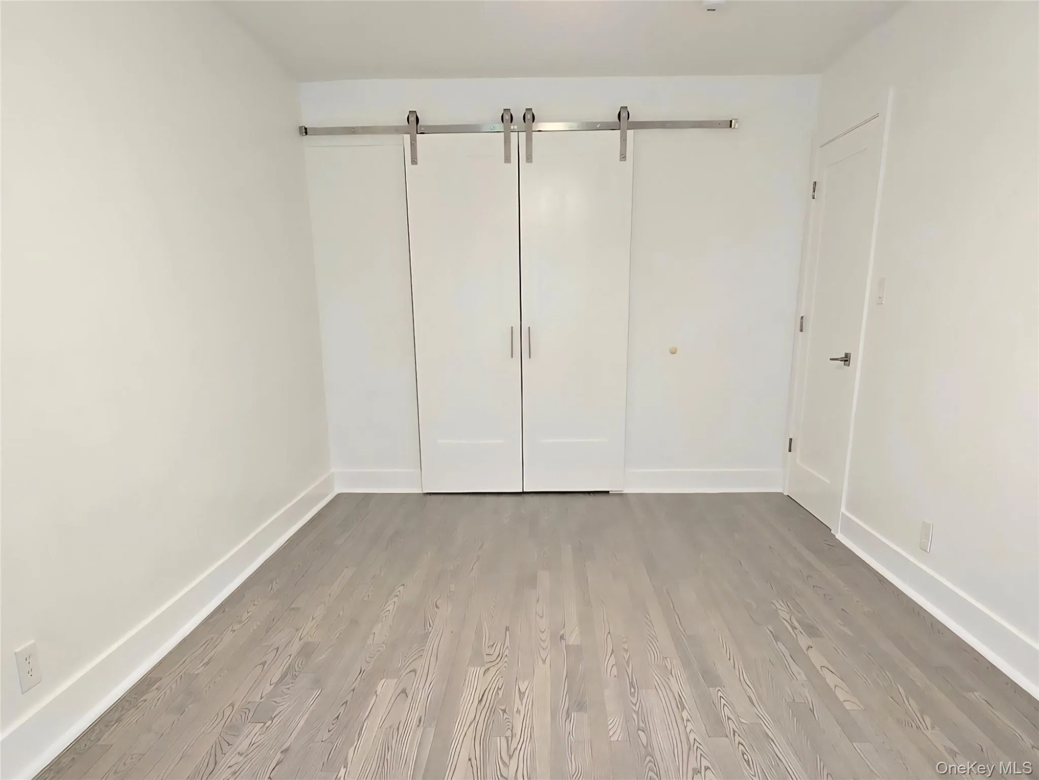 Unfurnished bedroom featuring a barn door and wood finished floors Unfurnished bedroom featuring a barn door and wood finished floors