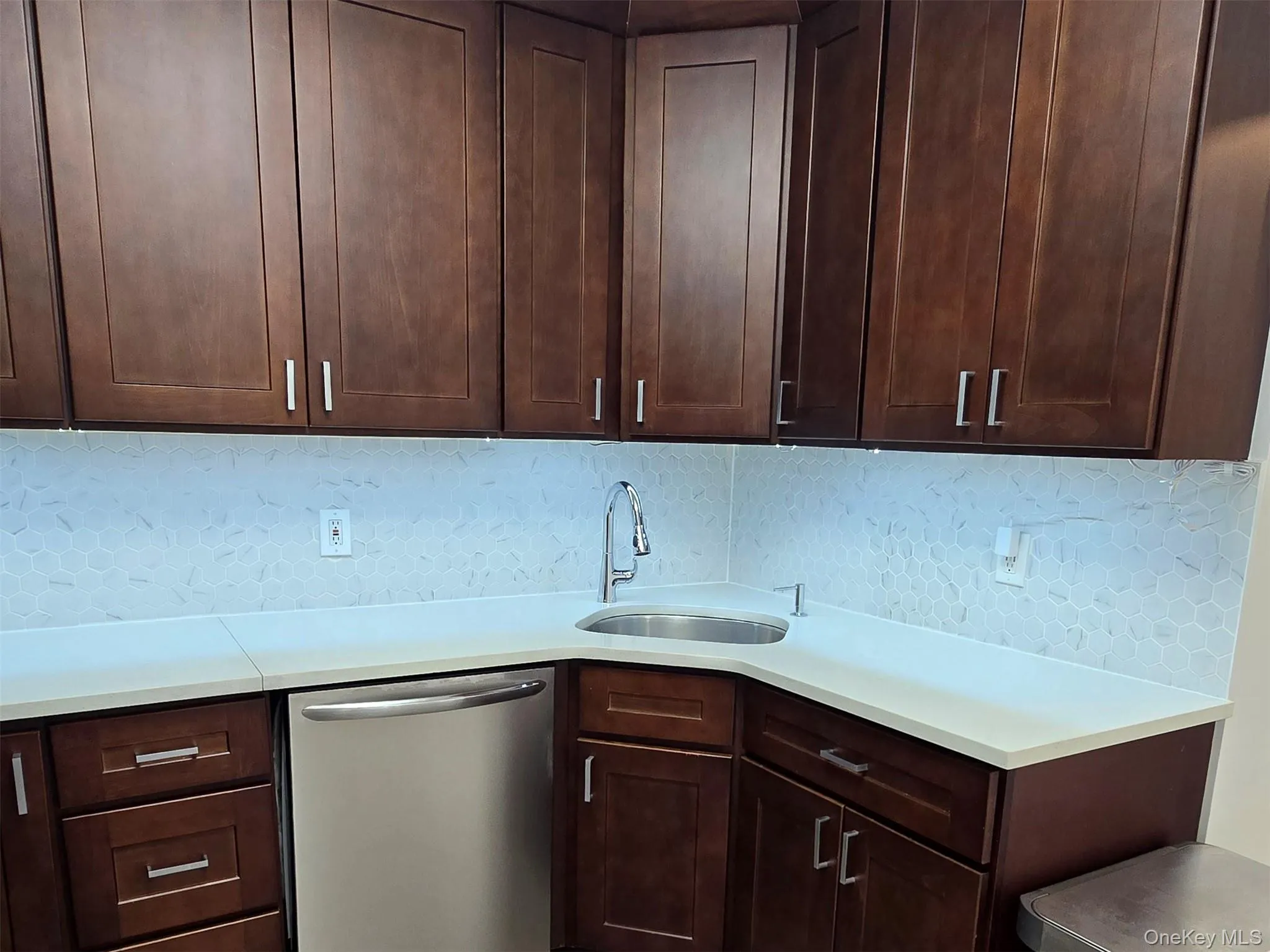 Kitchen with stainless steel dishwasher, dark wood cabinets, backsplash, and light Quartz counters Kitchen with stainless steel dishwasher, dark wood cabinets, backsplash, and light Quartz counters