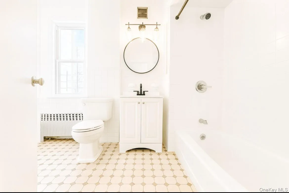 Bathroom with radiator, shower combination, vanity, tile walls, and a wainscoted wall Bathroom with radiator, shower combination, vanity, tile walls, and a wainscoted wall