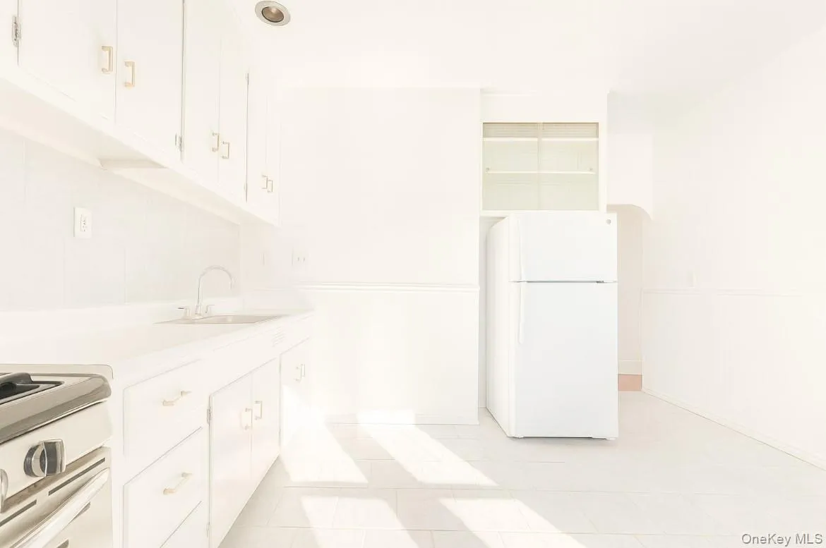Kitchen featuring freestanding refrigerator, light countertops, range with gas stovetop, and white cabinetry Kitchen featuring freestanding refrigerator, light countertops, range with gas stovetop, and white cabinetry