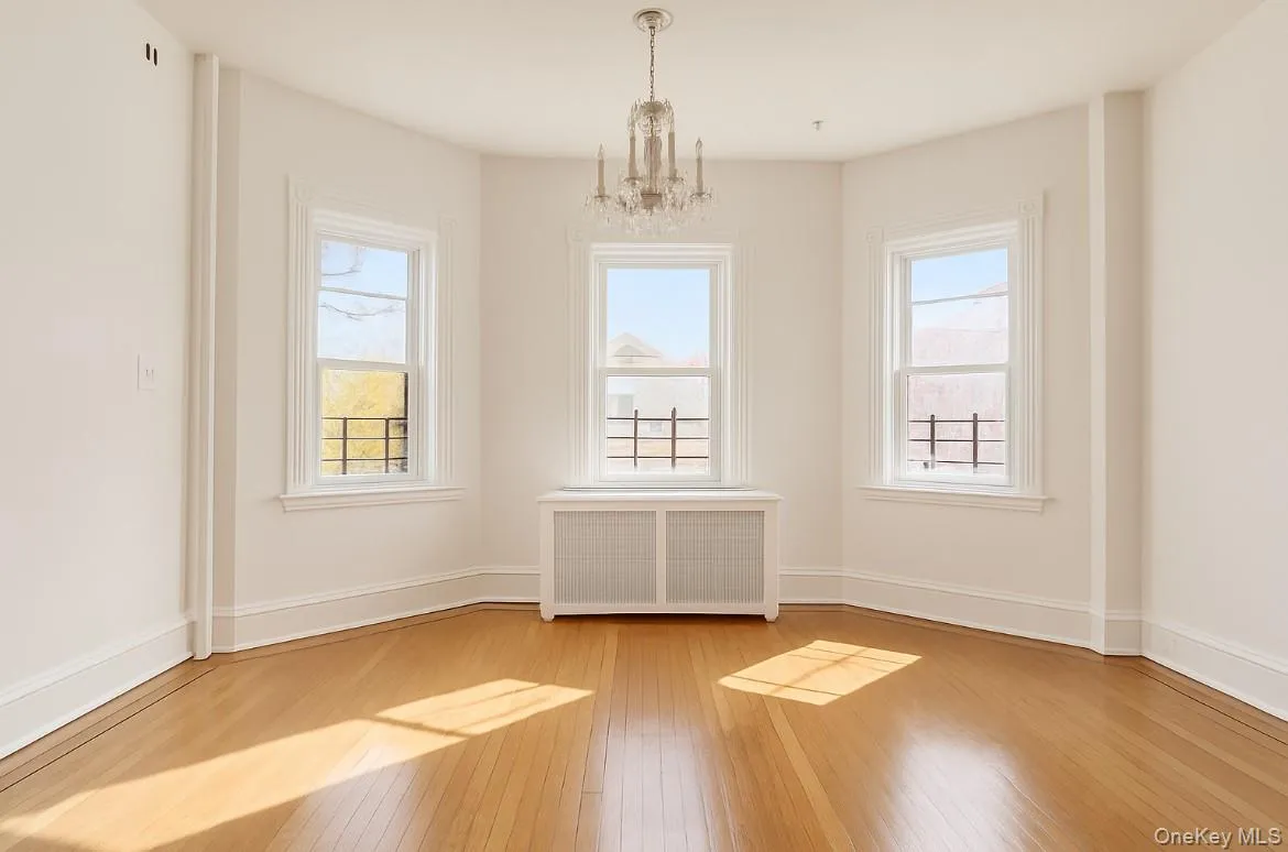 Empty room featuring radiator, a chandelier, healthy amount of natural light, and light wood-style flooring Empty room featuring radiator, a chandelier, healthy amount of natural light, and light wood-style flooring