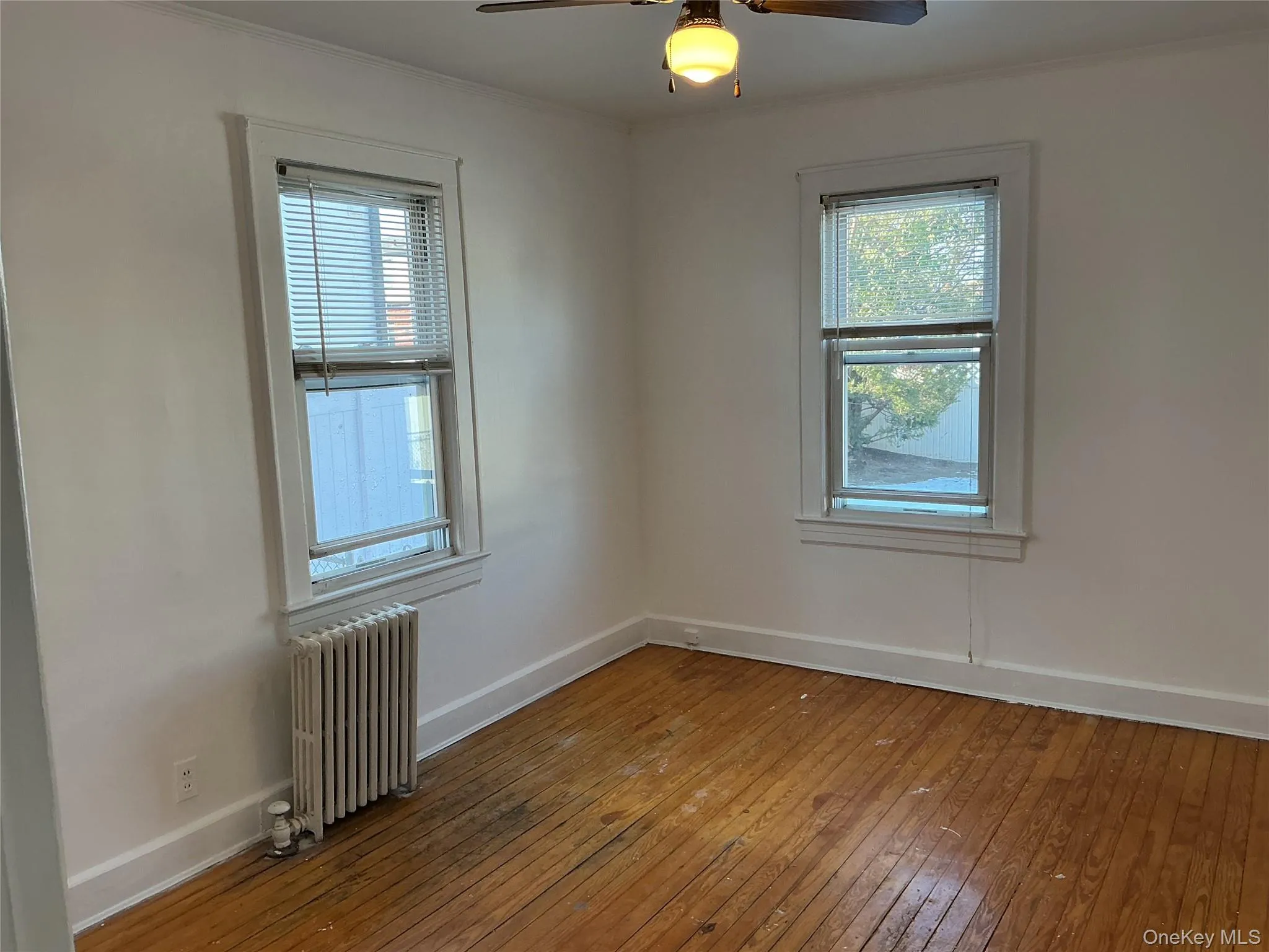 Empty room with radiator heating unit, hardwood / wood-style flooring, crown molding, and ceiling fan Empty room with radiator heating unit, hardwood / wood-style flooring, crown molding, and ceiling fan