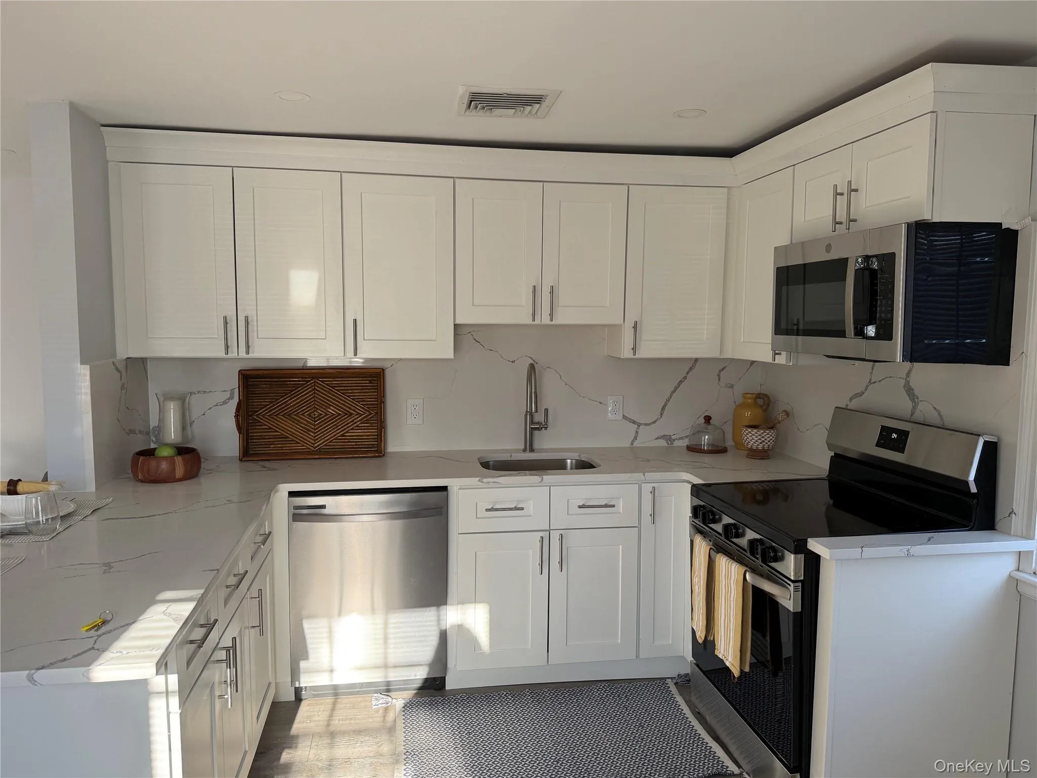 Kitchen with stainless steel appliances, white cabinets, light stone counters, and tasteful backsplash Kitchen with stainless steel appliances, white cabinets, light stone counters, and tasteful backsplash