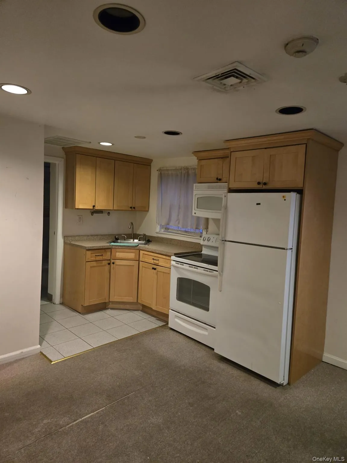 Kitchen with white appliances, light brown cabinets, light countertops, light carpet, and recessed lighting Kitchen with white appliances, light brown cabinets, light countertops, light carpet, and recessed lighting