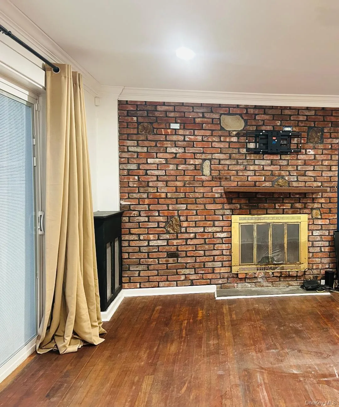 Unfurnished living room with a fireplace, dark wood finished floors, ornamental molding, and brick wall Unfurnished living room with a fireplace, dark wood finished floors, ornamental molding, and brick wall