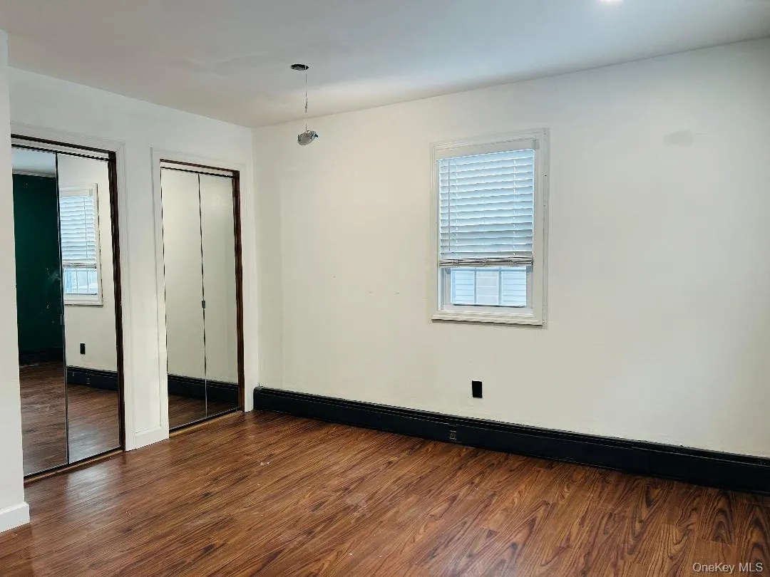 Unfurnished bedroom with multiple closets, dark wood finished floors, and baseboard heating Unfurnished bedroom with multiple closets, dark wood finished floors, and baseboard heating