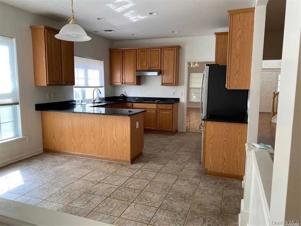 Kitchen with pendant lighting, a peninsula, brown cabinetry, under cabinet range hood, and recessed lighting Kitchen with pendant lighting, a peninsula, brown cabinetry, under cabinet range hood, and recessed lighting