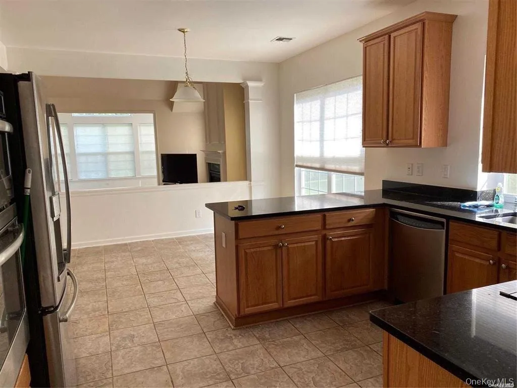 Kitchen with stainless steel appliances, brown cabinetry, pendant lighting, a peninsula, and dark stone countertops Kitchen with stainless steel appliances, brown cabinetry, pendant lighting, a peninsula, and dark stone countertops