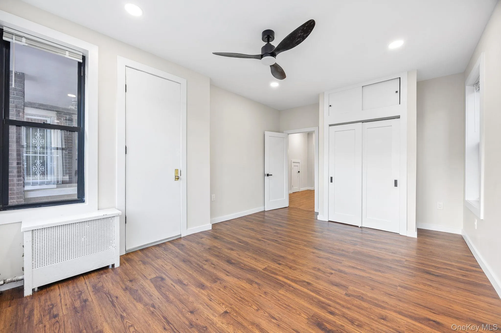 Unfurnished bedroom featuring multiple windows, radiator, dark wood-style floors, ceiling fan, and recessed lighting Unfurnished bedroom featuring multiple windows, radiator, dark wood-style floors, ceiling fan, and recessed lighting
