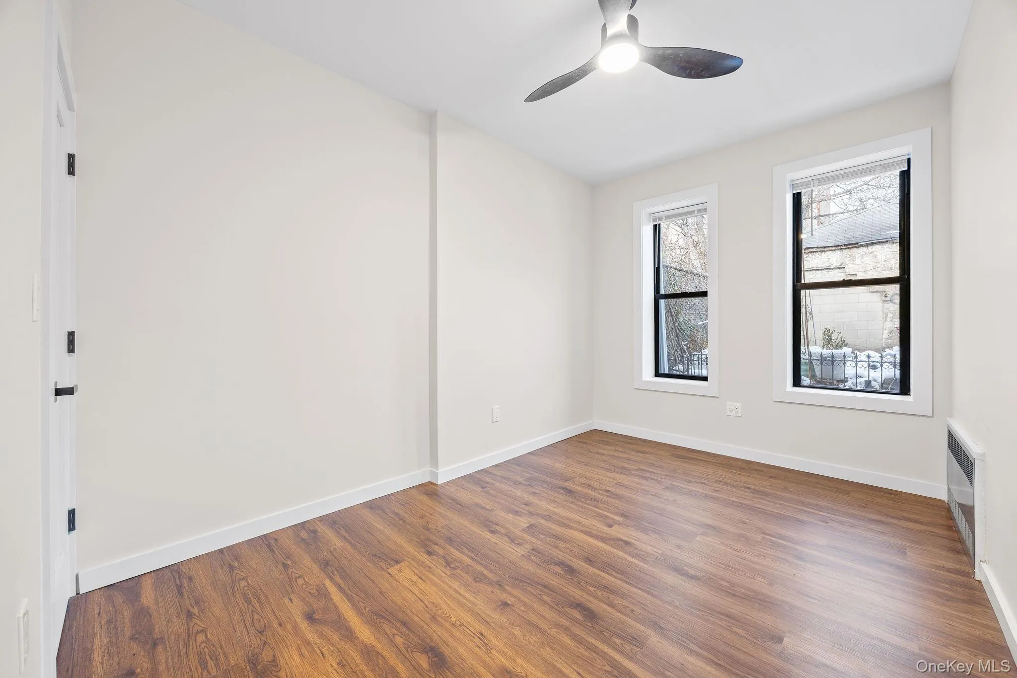 Empty room with dark wood-type flooring, radiator, and a ceiling fan Empty room with dark wood-type flooring, radiator, and a ceiling fan