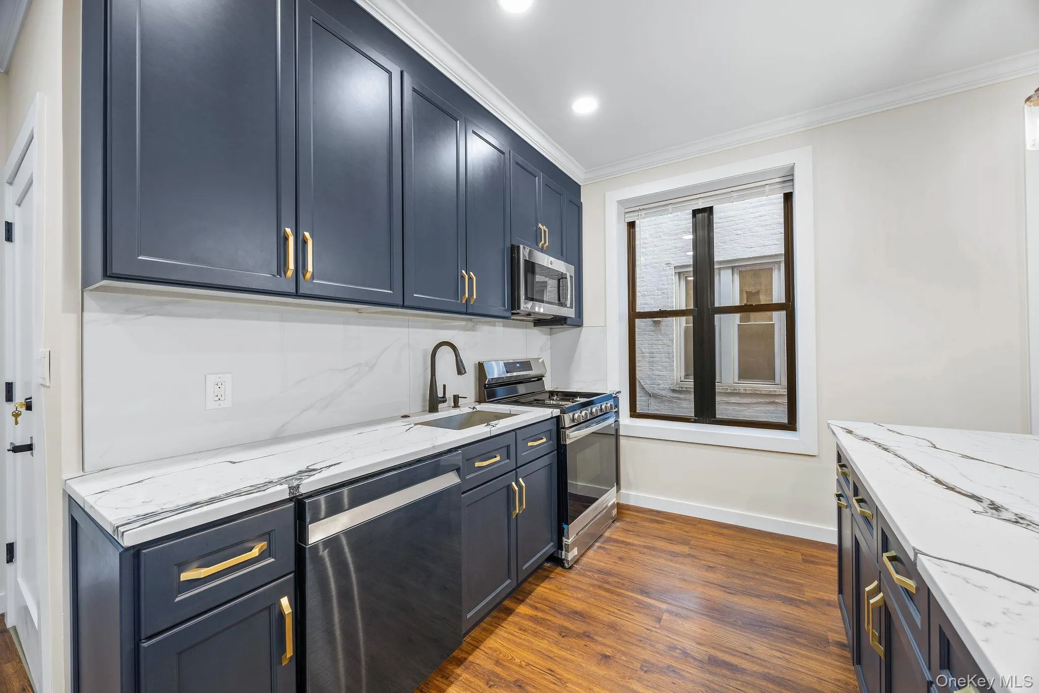 Kitchen with light stone countertops, stainless steel appliances, ornamental molding, dark wood finished floors, and blue cabinetry Kitchen with light stone countertops, stainless steel appliances, ornamental molding, dark wood finished floors, and blue cabinetry