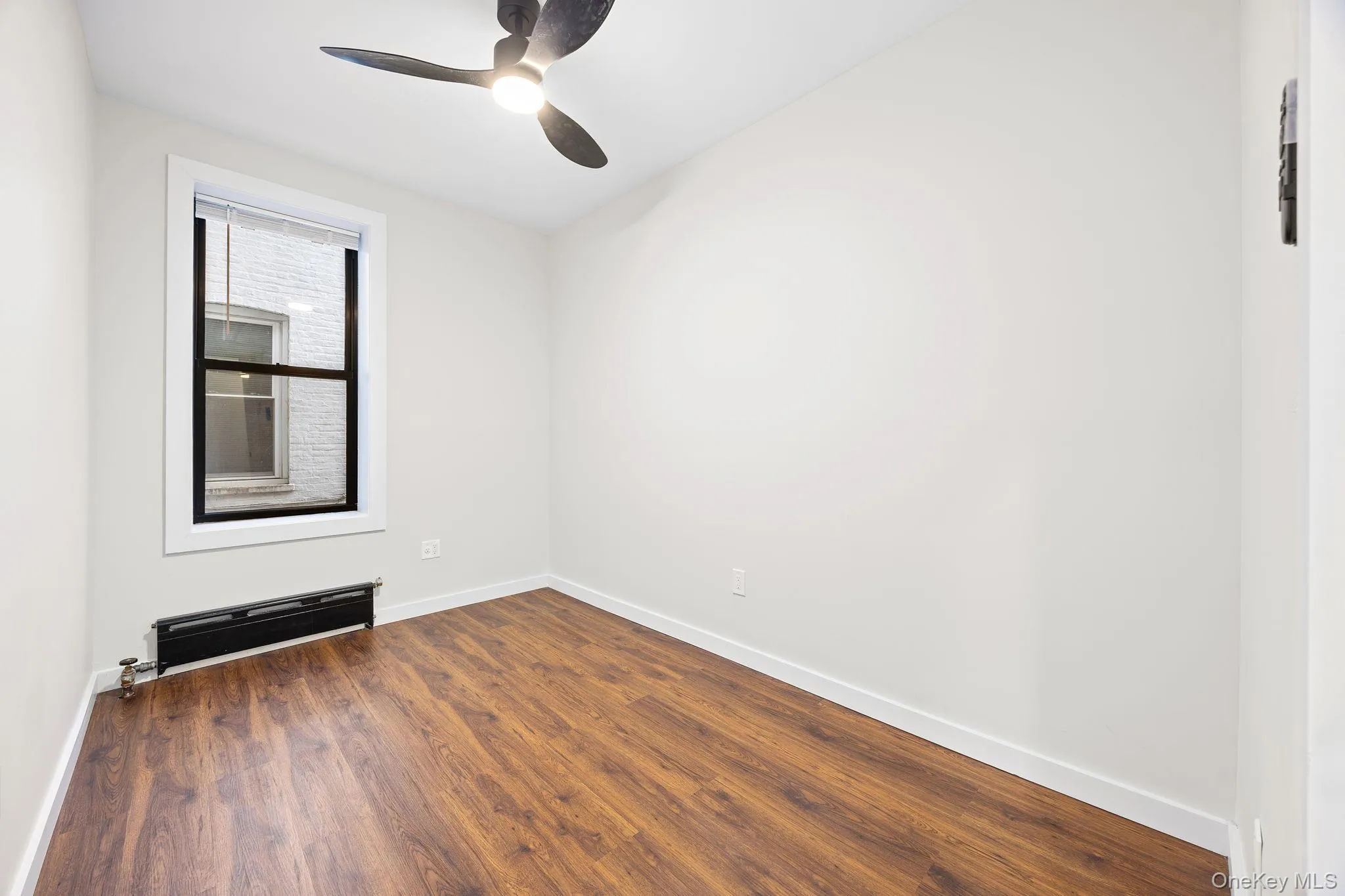 Empty room featuring a baseboard radiator, dark wood finished floors, and ceiling fan Empty room featuring a baseboard radiator, dark wood finished floors, and ceiling fan