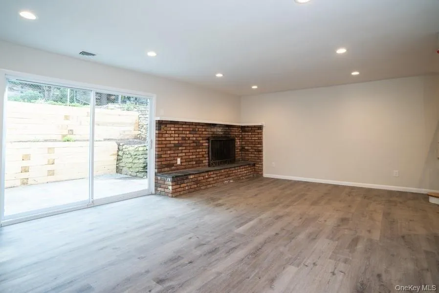 Unfurnished living room featuring recessed lighting, wood finished floors, and a brick fireplace Unfurnished living room featuring recessed lighting, wood finished floors, and a brick fireplace