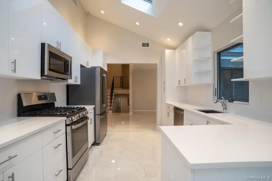 Kitchen with appliances with stainless steel finishes, open shelves, decorative backsplash, light marble finish flooring, and white cabinets Kitchen with appliances with stainless steel finishes, open shelves, decorative backsplash, light marble finish flooring, and white cabinets