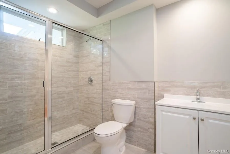 Full bathroom with vanity, a tile shower, tile walls, wainscoting, and recessed lighting Full bathroom with vanity, a tile shower, tile walls, wainscoting, and recessed lighting