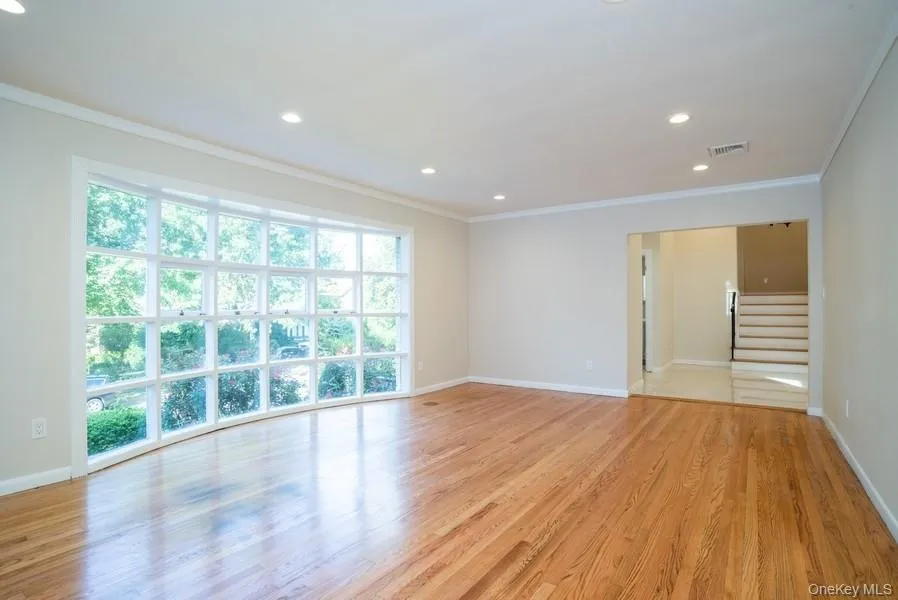Empty room with crown molding, stairs, light wood-type flooring, and recessed lighting Empty room with crown molding, stairs, light wood-type flooring, and recessed lighting