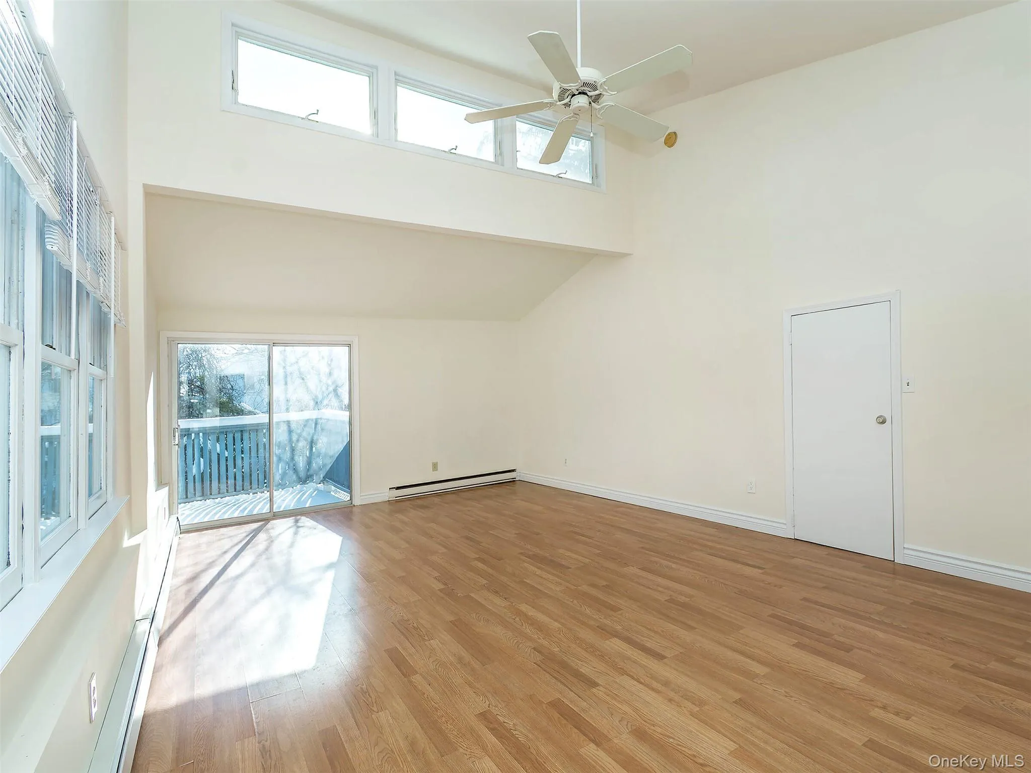 Unfurnished room featuring a towering ceiling, light wood-type flooring, a baseboard radiator, and a ceiling fan Unfurnished room featuring a towering ceiling, light wood-type flooring, a baseboard radiator, and a ceiling fan