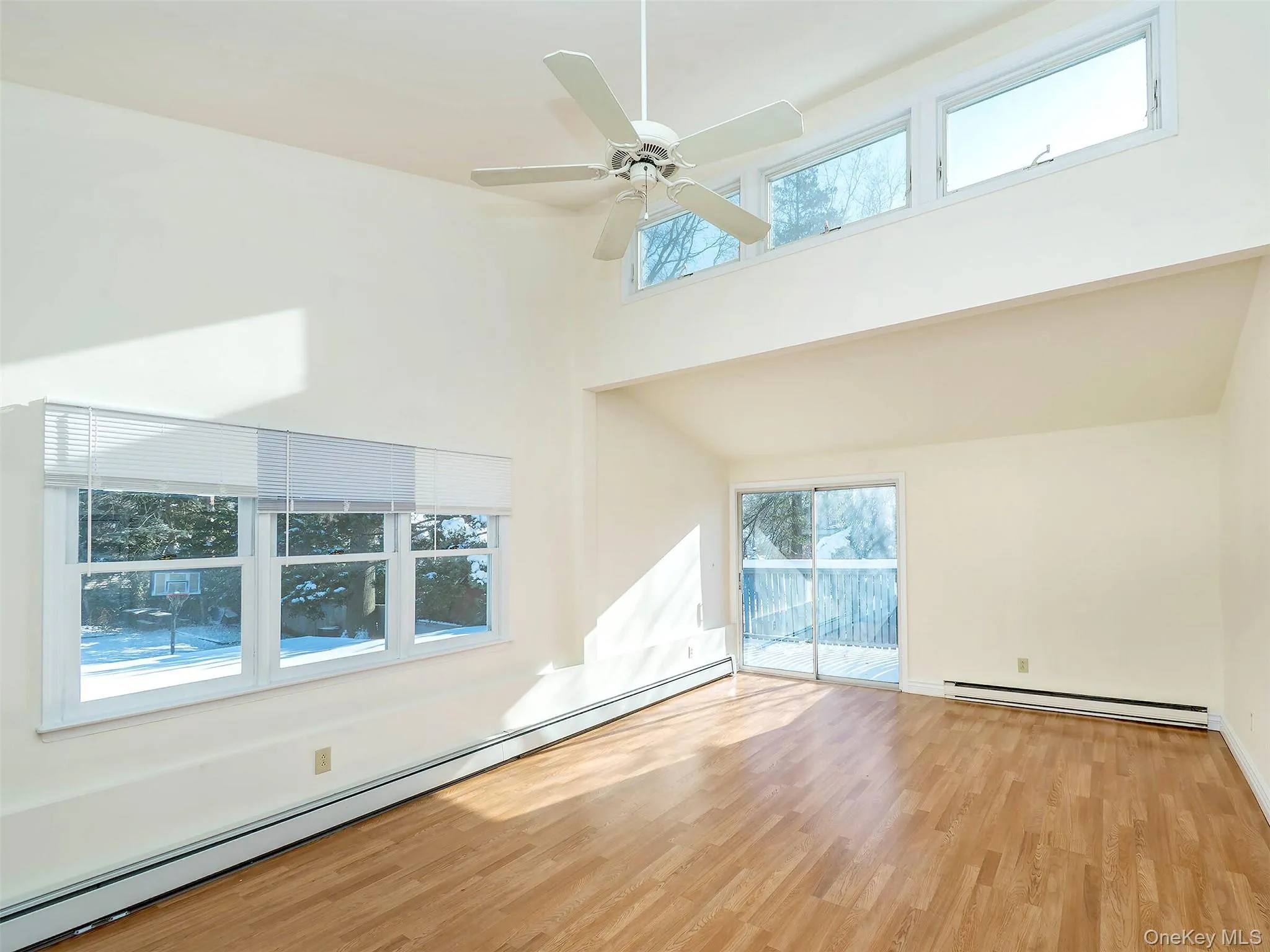 Unfurnished room with a baseboard radiator, a high ceiling, wood finished floors, a ceiling fan, and plenty of natural light Unfurnished room with a baseboard radiator, a high ceiling, wood finished floors, a ceiling fan, and plenty of natural light