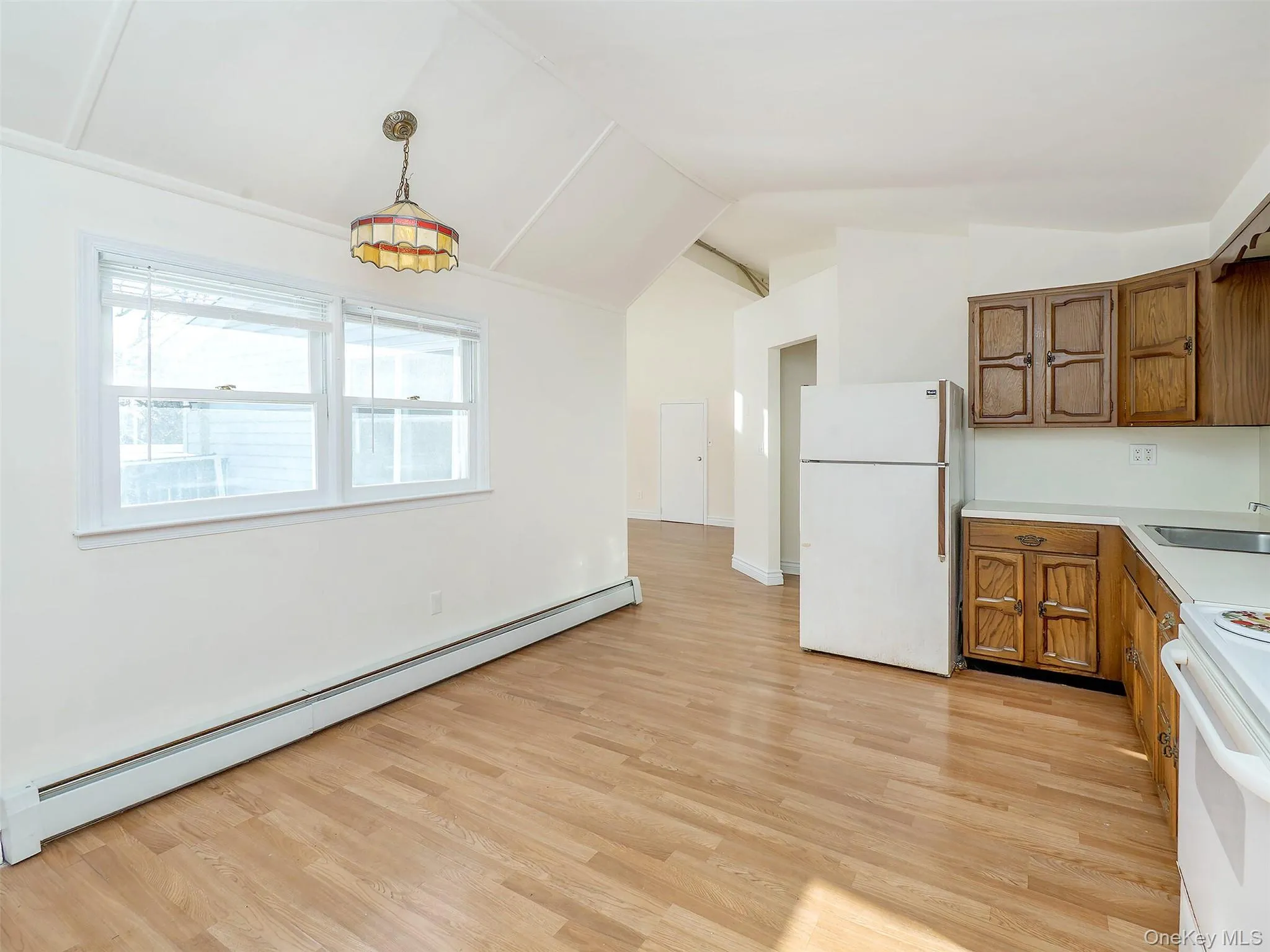 Kitchen featuring baseboard heating, white appliances, light countertops, brown cabinets, and vaulted ceiling Kitchen featuring baseboard heating, white appliances, light countertops, brown cabinets, and vaulted ceiling