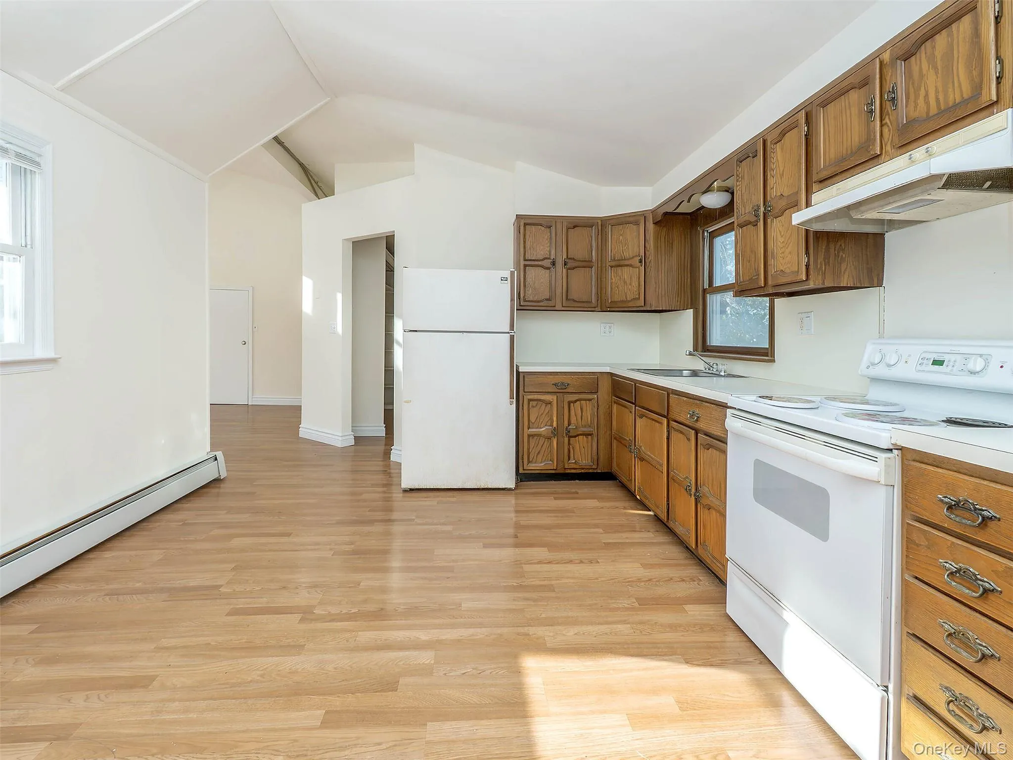 Kitchen with white appliances, brown cabinetry, lofted ceiling, under cabinet range hood, and light countertops Kitchen with white appliances, brown cabinetry, lofted ceiling, under cabinet range hood, and light countertops